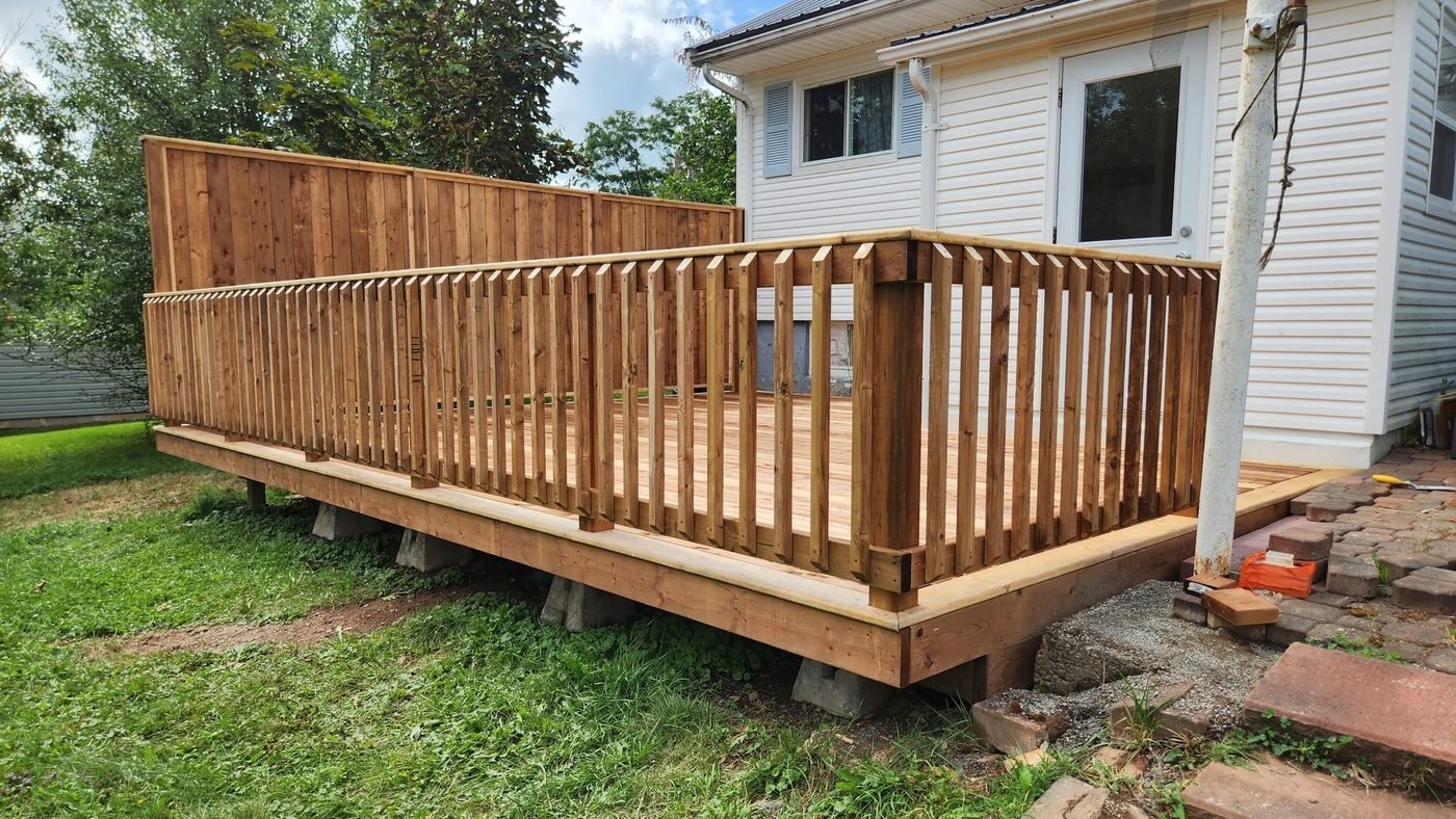 New wood deck with railing beside a house, built by Staged Right Carpentry